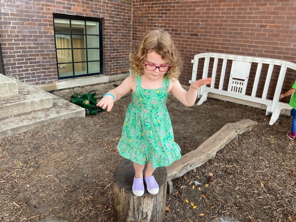 Early childhood student balances on a log in the garden, possibly preparing to jump off