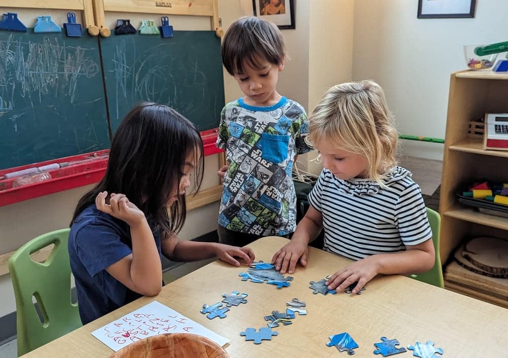 Early childhood students sit at a table and work on a puzzle